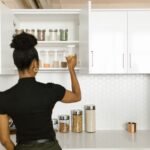 Kitchen cabinet organization ideas: a woman arranging jars and canisters inside neat white kitchen cabinets.