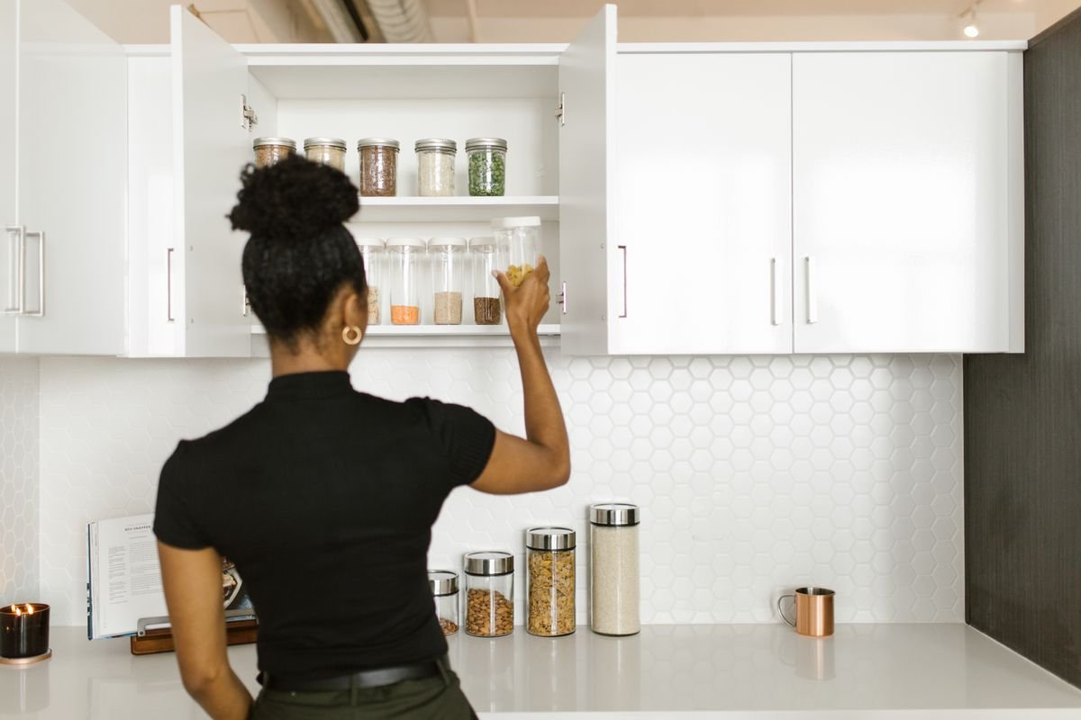 Kitchen cabinet organization ideas: a woman arranging jars and canisters inside neat white kitchen cabinets.