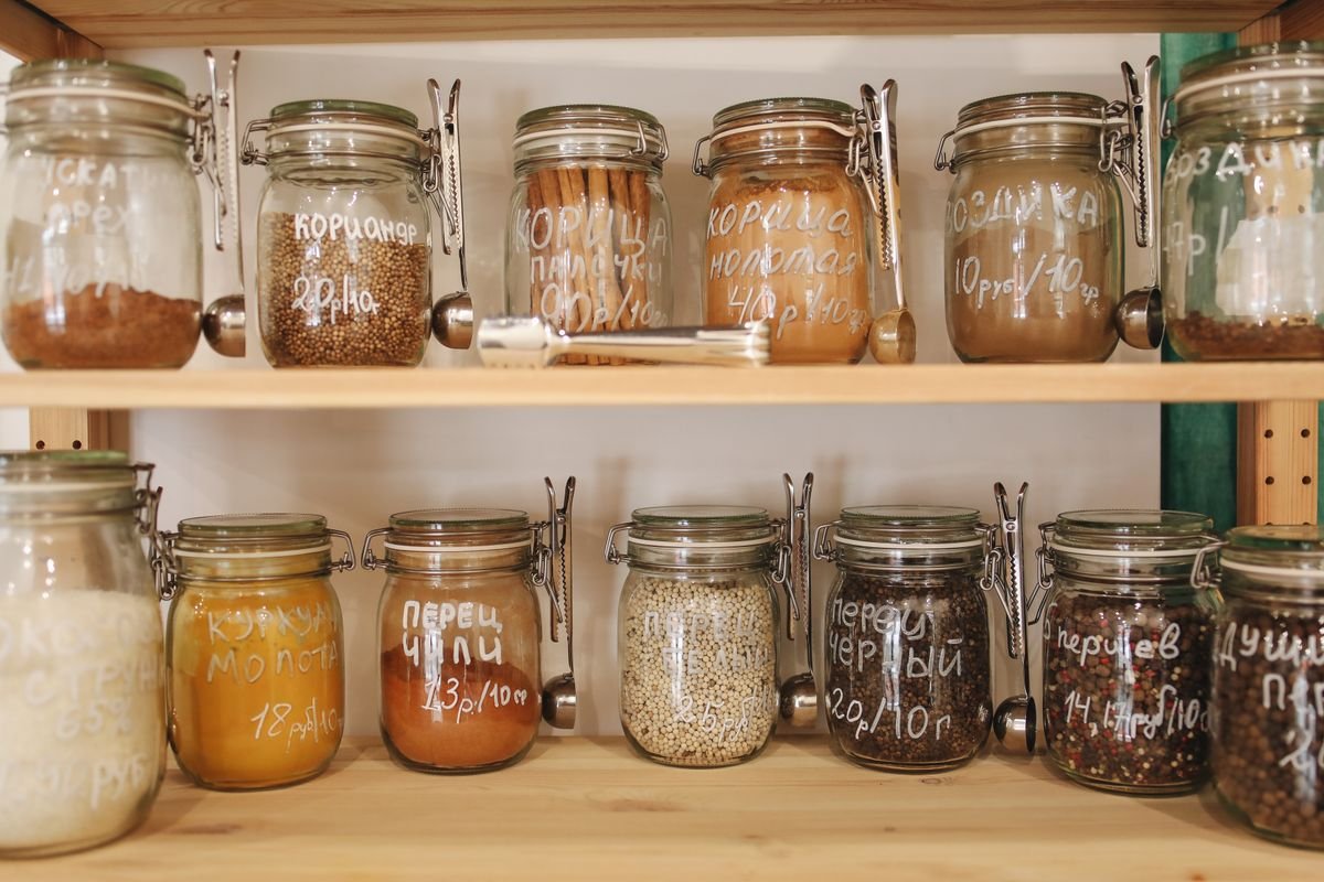 Kitchen cabinet organization ideas: spices in labeled glass jars lined up in one layer on wooden cabinet shelves.