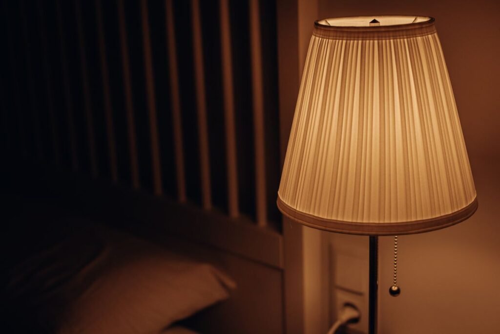 Warm, dim bedside lamp lighting the sleep zone in a studio apartment layout, kept separate from the brighter work light