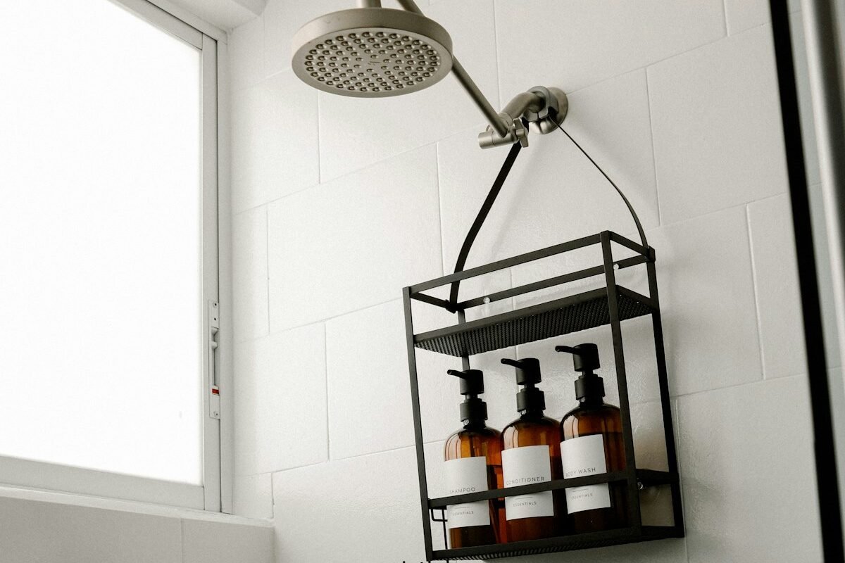 Small bathroom storage ideas no counter space: a black metal caddy hanging from the showerhead holding amber toiletry bottles